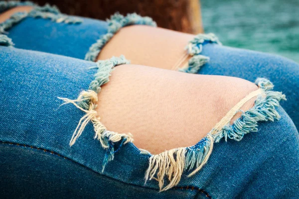 Jeans com dois grandes buracos e pedaços de fio no joelho — Fotografia de Stock