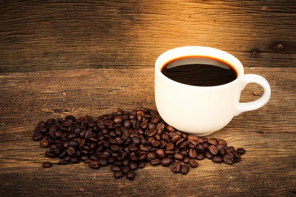 Filiżanka kawy z ziaren kawy na starej drewnianej podłodze. — Zdjęcie stockowe