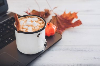 Beyaz ahşap arka planda şekerleme, balkabağı, akçaağaç yapraklı sıcak çikolata kupası.