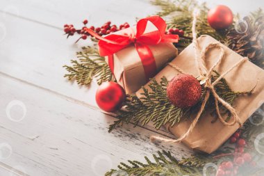 Kırmızı kurdeleli ve köknar dallı Noel hediyeleri kutuları, beyaz ahşap arka planda kırmızı Noel topları