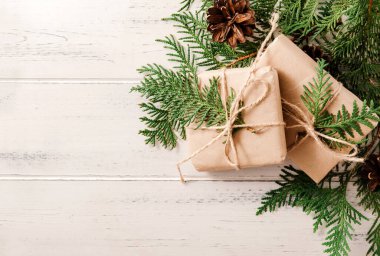 Beyaz ahşap arka planda köknar dalları ve konileri olan 2 Noel hediyesi kutusu.