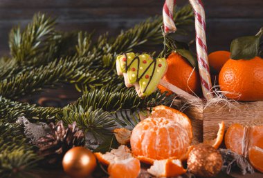 Mandalina dilimleri, mandallar, köknar dalları, altın Noel topları, lolipop, siyah ahşap arka planda kurabiyeler.