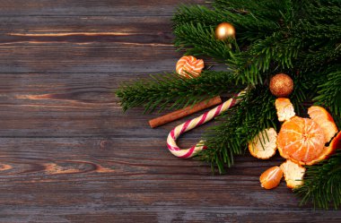 Mandalina, ladin dalı, lolipop, tarçın çubuğu, koyu ahşap arka planda altın Noel topları.