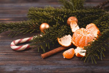 Mandalina, lolipop, tarçın çubuğu, ladin dalı, koyu ahşap arka planda altın Noel topları.