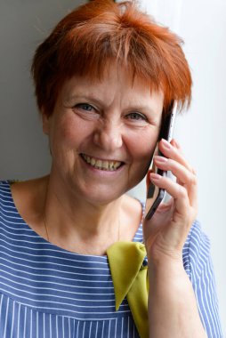 60 yaşında yetişkin bir kadın telefonda konuşuyor ve gülümsüyor.