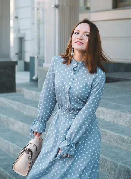 1 white young woman with red hair in a gray dress close-up, girl smiling, standing on the street 1 white young woman with red hair in a gray dress close-up,