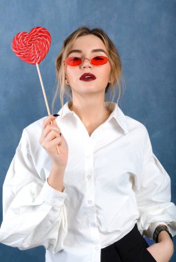 Beyaz tişörtlü, kırmızı gözlüklü, gri arka planda kırmızı kalpli 1 beyaz sarışın kadın.