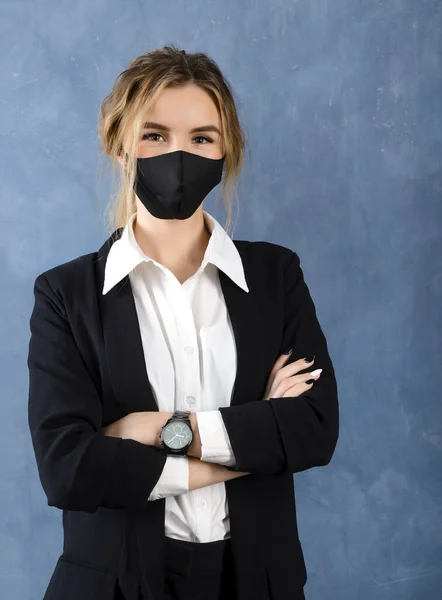 european blonde woman in black mask, white shirt and black jacket on gray background close up, female portrait