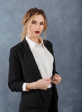 Beyaz tişörtlü, siyah ceketli, gri arka planda 1 beyaz sarışın kadın.