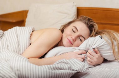 Bir tatlı beyaz kız yatağında gözleri kapalı ve gülümsüyor.