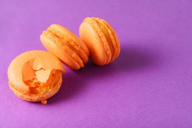 Mor arka planda 3 şeftali sarısı badem kurabiyesi.