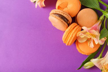 şeftali sarısı badem kurabiyeleri mor arka planda, alstromerya çiçekleri üstte.
