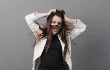 Beyaz ceketli beyaz kadın mutlu, deli, uzun saçlı ve gözlüklü bir iş kadını gri arka planda gülüyor.