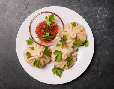 Domates soslu khinkali, arka planda koyu renkli otlar, hamur tatlısı.