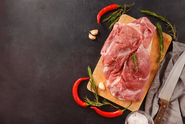 raw pork shoulder, tenderloin with chili pepper, rosemary, knife, napkin on a black background, red meat