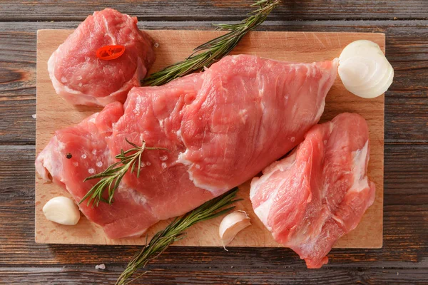 raw pork tenderloin, rosemary, onion, garlic on a wooden background
