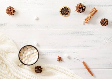 Marşmelovlu bir fincan sıcak çikolata, köknar kozalakları, tarçın çubukları, beyaz ahşap arka planda beyaz bir süveter, yazıtlar için bir yer, üst görünüm.