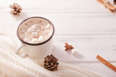 Marşmelovlu sıcak çikolata, tarçın çubukları, köknar kozalakları, beyaz ahşap arka planda beyaz süveter, yazıtlar için bir yer, üst görünüm.