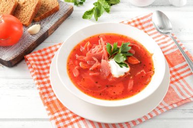 Ekşi kremalı kırmızı Rus çorbası ve beyaz bir tabakta beyaz tahta bir masada beyaz bir tabakta otlar.