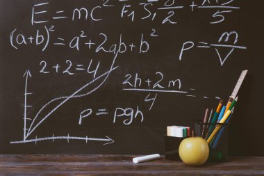 Formüller, karatahtadaki tebeşirler, kalemler, elmalar, kalemler, masanın üzerine.,