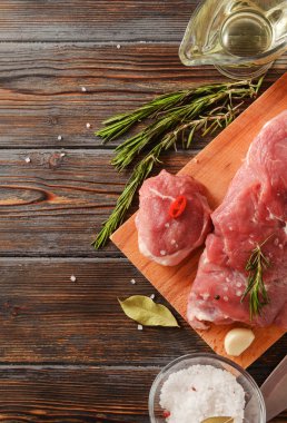 Kesme tahtasında biberiyeli çiğ domuz filetosu, siyah ahşap arka planda tuz.