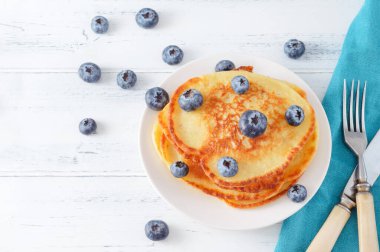 Yaban mersinli gözlemeler açık ahşap bir masada, çatal, bıçak, mavi peçete, üst manzara