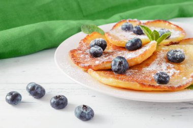 Yaban mersinli krep, pudra şekeri ve nane şekeri tabakta, beyaz arka planda yeşil peçete.