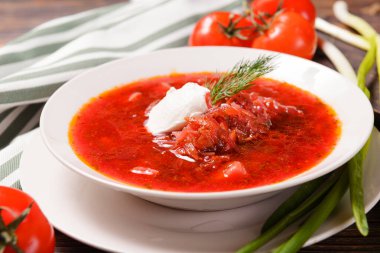 Ekşi kremalı Ukrayna çorbası ve beyaz bir tabakta dereotu, soğan, domates 