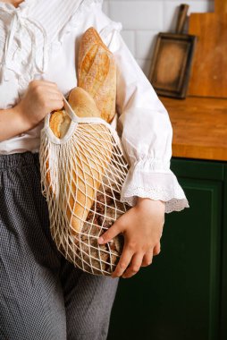 Mutfakta çantasında ekmek olan beyaz bluzlu bir kadın.