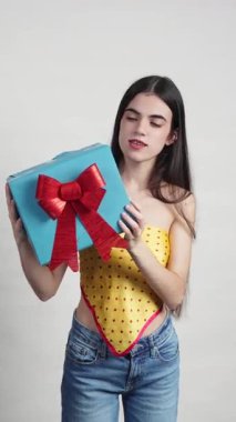 Beyaz arka planda izole edilmiş bir hediyeyi sallayan telleri olan neşeli genç bir kadın.