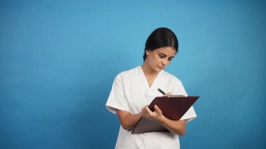 Beyaz üniformalı profesyonel kadın hemşire hasta bilgilerini dikkatlice panoya yazıyor.