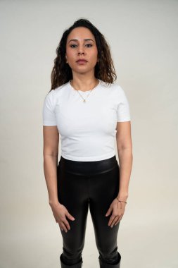 Tarafsız bir ifadeyle, beyaz tişört ve siyah tayt giyen bir kadın.