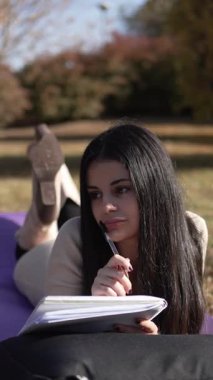 Düşünceli bir öğrenci güneşli bir sonbahar gününde çimlere uzanıp günlüğünü yazıyor.