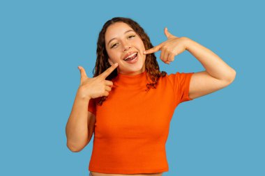 Sağlıklı dişlerini gösteren genç bir kadın ve mavi arka planda neşeli bir gülümseme.