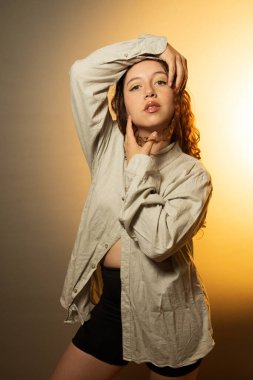 Stüdyoda poz veren genç bir kadın, kendine güvenini ve tarzını ılık bir ışıkla gösteriyor.