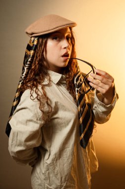 Benzersiz moda tarzıyla poz veren genç bir kadın ve sıcak ışığa karşı kıvırcık saçlı.