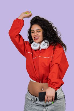 Kıvırcık saçlı neşeli kadın müzikten zevk alıyor, neşe ve tasasız yaşam tarzı gösteriyor.