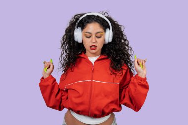 Kablosuz kulaklıkla müzikten hoşlanan genç bir kadın mor arka planda sallanıyor.