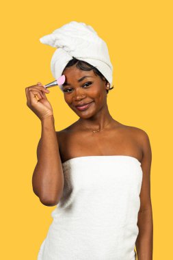 Kadın güzellik gösterisi yapıyor, sarı arka planda cilt bakımı için toz makyaj yapıyor.