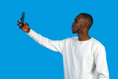 Afrikalı bir adam mavi arka planda cep telefonuyla bir anı yakalıyor.