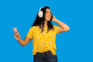 Gülümseyen, dans eden, kulaklıklı ve akıllı telefonlu müzikten hoşlanan genç bir kadın.