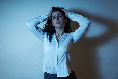 Stresli bir kadın mavi bir ışığın altında ellerini tutarak hayal kırıklığını ifade ediyor.