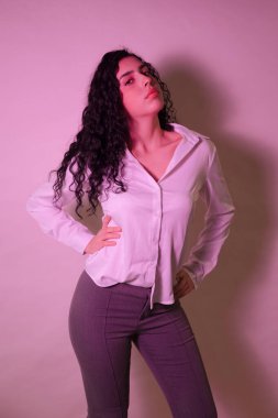 Kalçasında elleri olan, kendine güvenen ve stüdyoya dik dik bakan genç bir kadın.
