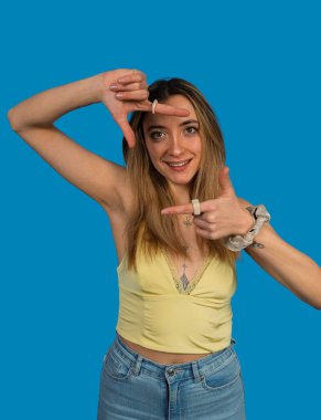 Genç bir kadın, mavi arka planda kameraya gülümsüyor.