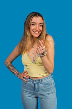 Kameraya gülümseyen ve kalp işareti yapan genç bir kadın.