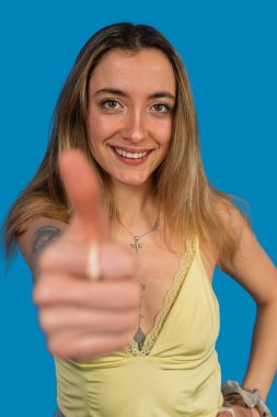 Gülümseyen kadın mavi arka planda olumlu bir hareketle onaylıyor.