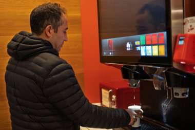 Modern bir içecek çeşmesinde bir bardağı soğuk içecekle dolduran adam.