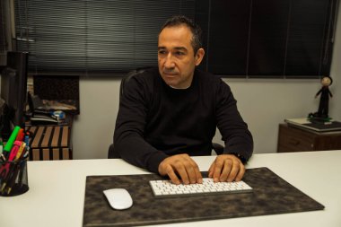 Ofis masasında bilgisayar başında çalışan olgun bir adam, odaklanmış görünüyor.