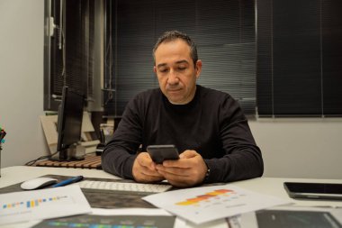 Ofis masasında akıllı telefonuna odaklanan bir adam.