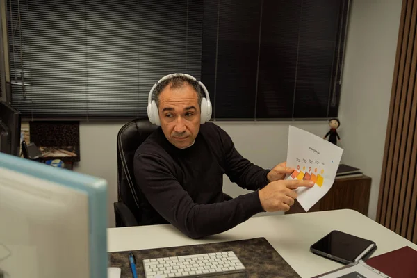 İnternetteki bir video konferansı sırasında kulaklıklı bir işadamı grafiğe bakıyor.